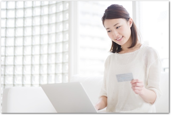 キャッシュカードを手にパソコンでネットショッピングをする女性
