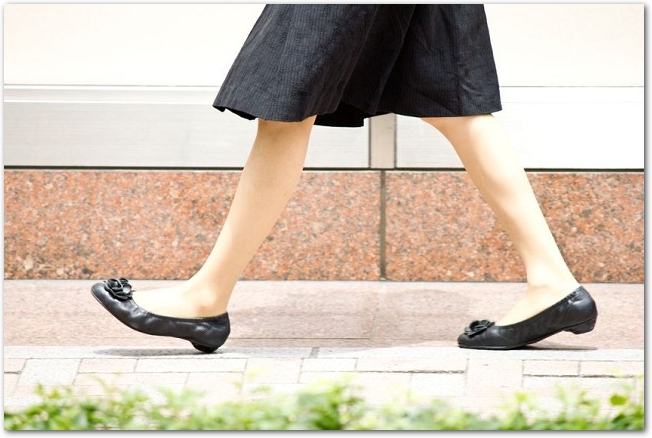 街中の歩道を歩いているスカートを履いた女性の脚